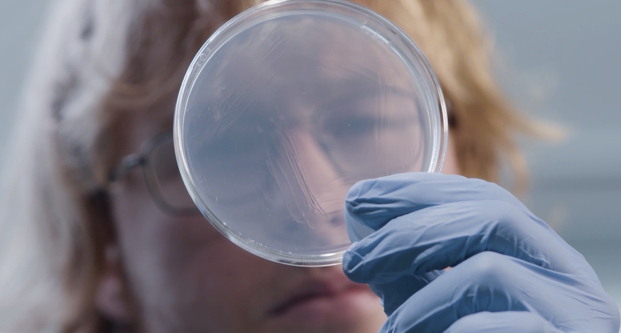 This image shows a female researcher looking through a petri dish .jpg